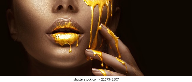 Gold Paint Smudges Drips From The Face Lips And Nails, Lipgloss Dripping From Sexy Lips, Golden Liquid Drops On Beautiful Model Girl's Mouth, Gold Metallic Skin Make-up. Beauty Woman Makeup Close Up.