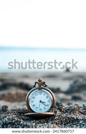 Gold pocket watch lies on a sandy beach with blurry beach waves in the background. With copy space for text