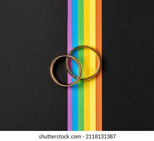 Gold Rings For Lesbian And Gay Wedding And Rainbow Ribbon On Black Table