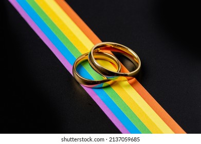 Gold Rings For Lesbian And Gay Wedding And Rainbow Ribbon On Black Table