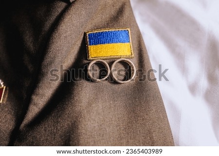 Gold rings lie on the uniform of the Ukrainian military, soldier with the flag of Ukraine. Close-up wedding photography.