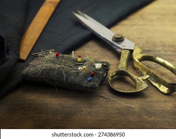 Gold scissors pin cushion, and black fabric.Measuring, cutting, sewing textile or fine cloth. Work table of a tailor. Shallow depth of field, Focus in on  pin on the pin cushion.