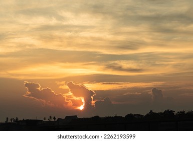Gold setting sun behind the clouds on orange sky at dramatic sunset. Evening sky scene with golden light from the setting sun, Last light of the day. Abstract natural pattern background, Copy space.
