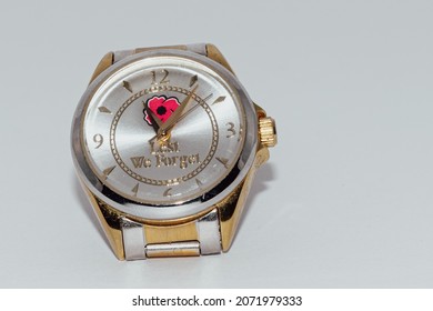 A gold and silver watch set to eleven minutes after eleven o'clock. It says Lest We Forget and has a red poppy on it.