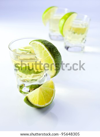 gold tequila with lime on a white reflective background.