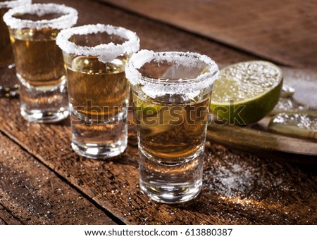 Gold tequila shots with lime fruits on wooden background