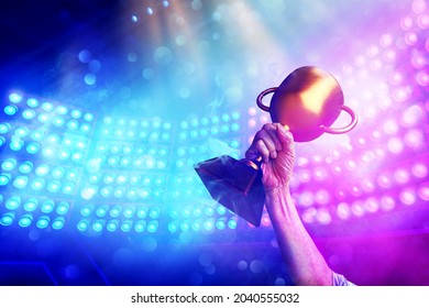  Gold trophy in winner 's hand with background spotlight on e-sport competition stage in the stadium , win concept.  - Shutterstock ID 2040555032