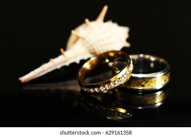 Gold wedding ring and shell on black background