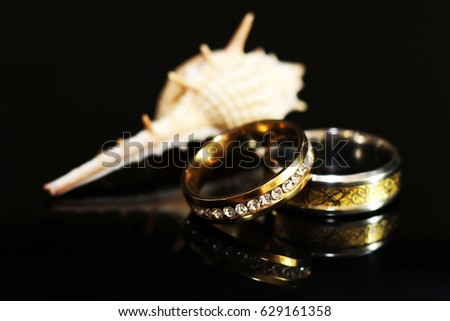 Gold wedding ring and shell on black background