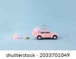 Gold wedding rings on miniature toy retro car decorated with pink flowers on blue background. The concept of marriage. Copy space.