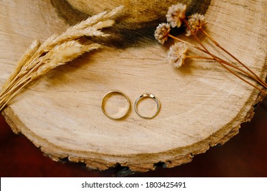 Gold Wedding Rings On A Wooden Cut With Spikelets And Dried Flowers.