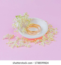 gold wedding rings in a white seashell with beautiful white elderflower flowers on a pink pastel background