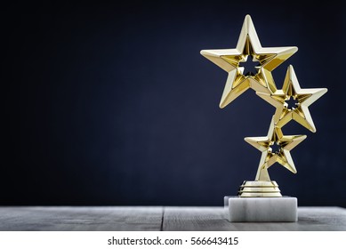 Gold winners award with three stars to be awarded to the first place in a competition or championship standing on a pedestal against a blue background with copy space