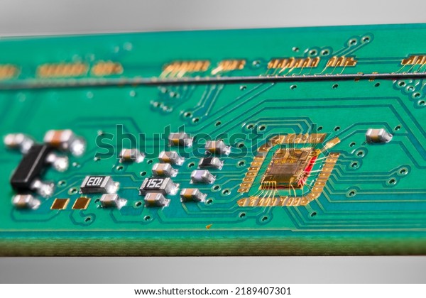 Gold wires of chip bonding to green PCB detail\
from flatbed scanner on a gray background. Integrated circuit die\
wired to electronic printed board with surface mounted components\
and line scan camera.