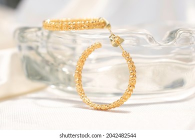 Gold Woven Hoop Earrings.  They Are On A Glass Ashtray