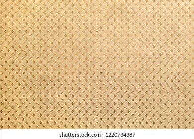 Golden background from metal foil paper with a pattern of sparkling stars closeup. Texture of yellow metallized wrapping holiday paper surface.
