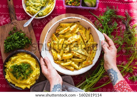 Golden baked fried potato sticks or slices with rosemary and thyme. Woman holds in hands homemade vegan food.