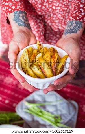Golden baked fried potato sticks or slices with rosemary and thyme. Woman holds in hands homemade vegan food.