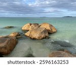 Golden big boulders sunbathed by the late afternoon sun. Brown and orange stones, green turquoise sea, sky full of gray and white clouds, mountains in the horizon. Jurere Internacional beach.