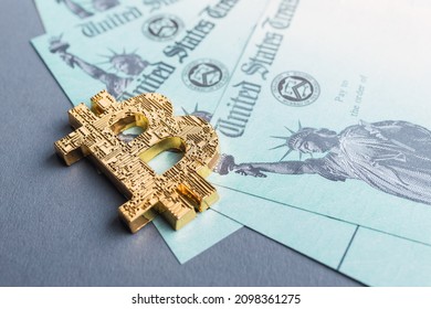 A Golden Bitcoin Symbol Laying On A Group Of IRS Stimulus Refund Payment Checks