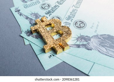 A Golden Bitcoin Symbol Laying On A Group Of IRS Stimulus Refund Payment Checks