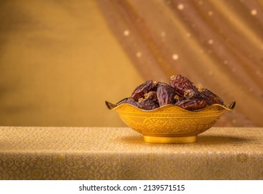 A golden bowl filled with fine quality Arabian dates. A studio shot of sacred date fruits against golden background with clear space for text.