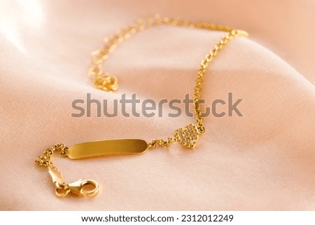Golden bracelet with name plate, heart and diamond on a pink background. Romantic decorations. Сoncept for Valentine's Day
