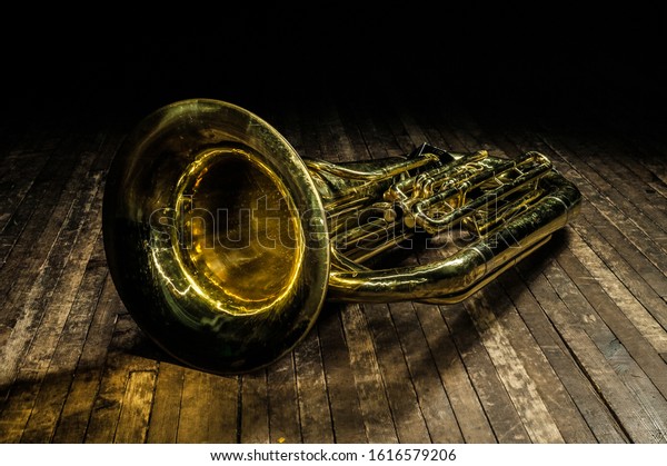 golden brass wind instrument
euphonium lies on a brown wooden stage in the light of a
spotlight