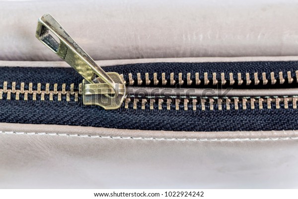Golden brass zipper on a\
leather bag. selective focus. The zipper is device consisting of\
two flexible strips of metal with interlocking projections closed\
or opened.