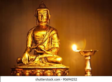 Golden Buddha statue on altar with oil lamp with flame