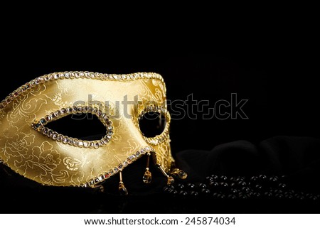 Golden carnival mask near pearls on black background