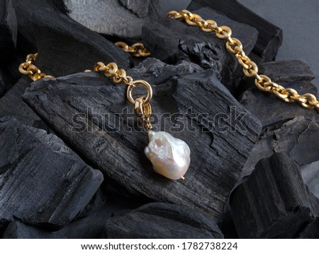 Golden chain with white baroque pearl pendant on black coal background. Close-up shot