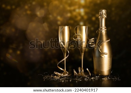 golden champagne bottle and two glasses with ribbons on black bokeh background. new year and anniversary celebration. copy space