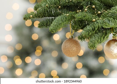 Golden Christmas Balls Hanging On Fir Tree Against Blurred Festive Lights