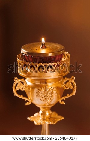 A golden church candlestick for one kerosene candle close-up on a dark warm background. Church paraphernalia.