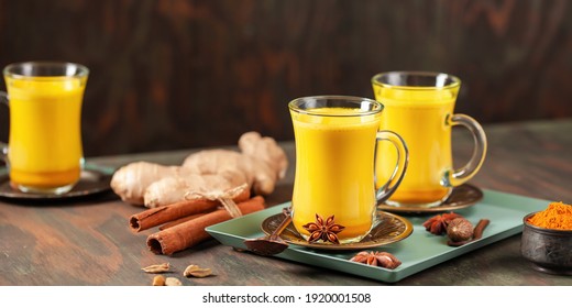 Golden Cinnamon  Turmeric Milk. Trendy hot Healthy drink with turmeric roots and spices. Indian Masala Haldi Doodh. Wooden background. Banner