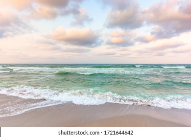 golden cloudy sunset above the green sea waters. waves crashing the sandy beach. clear horizon. changing windy weather