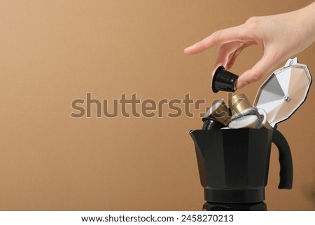 Golden coffee capsules in coffee maker and hand on beige background, space for text