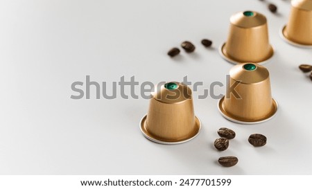 Golden coffee capsules and scattered beans on a white background. Copy space