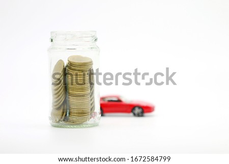 Golden coils collection in jar with blurry red super car behind on white background, saving for dream concept.