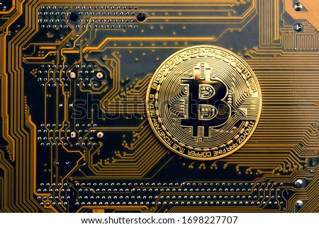 A golden coin with bitcoin symbol on a mainboard.