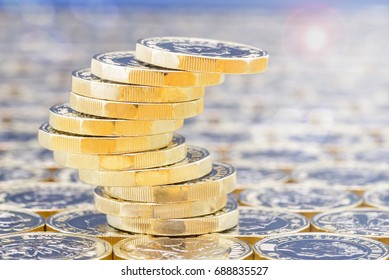 Golden coins with light effects. British pound coins in a precarious stack on a background of more money with lens flare and light filters.