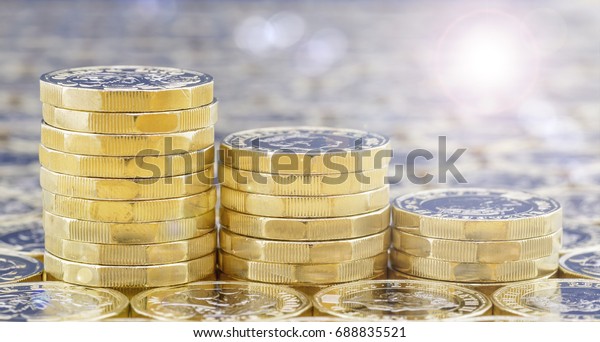 Golden coins with light effects. British pound
coins in three descending stacks on a background of more money with
bright sunlight light
filters.