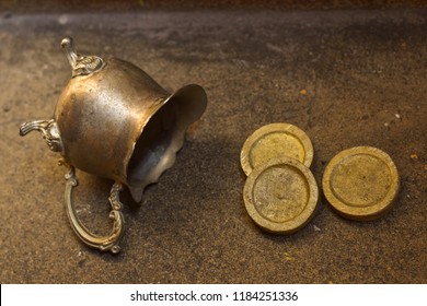 Golden coins out off a little pot on a stone gorund under the natural light of the sun.