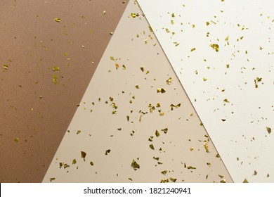 Golden Confetti On Earthy Brown, Beige And White Paper Geometric Trendy Background. Festive Holiday Backdrop. Birthday Congratulations Christmas New Year. Flat Lay, Top View, Copy Space.