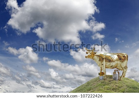 A golden cow on top of a grassy hill against a cloudy blue sky, for the concept of financial cash cow.