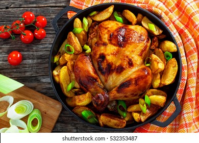 golden crispy skin chicken grilled in oven with potato wedges and leek in cast iron pan on old wooden boards, chopping board with slices of onion and cherry tomatoes on background,  view from above - Powered by Shutterstock