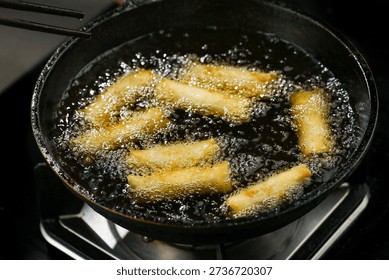 Golden crispy spring rolls deep frying in bubbling oil, creating delicious dim sum appetizers with perfectly fried veggie-filled wrappers