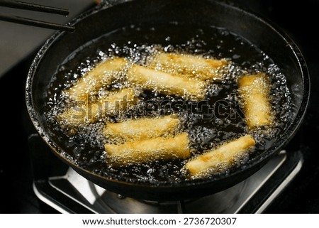 Golden crispy spring rolls deep frying in bubbling oil, creating delicious dim sum appetizers with perfectly fried veggie-filled wrappers