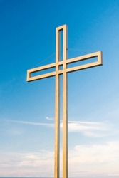 Golden Cross Against A Background Of Blue Sky With Clouds. A Minimalistic View Of A Gold-colored Cross Against The Sky.